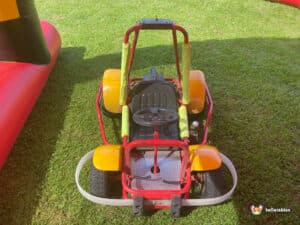 A small go-kart parked on a patch of green grass, showcasing its vibrant colors and compact design.