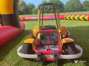 A small go-kart is parked on green grass, displaying its vibrant colors and compact form in a natural setting.