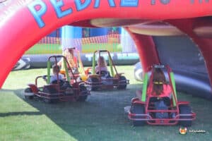 Children in colorful go-karts on a grassy field, engaged in a spirited race under a clear blue sky.