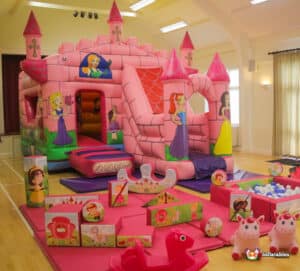 A vibrant pink castle bouncy structure, complemented by soft play items, perfect for an enchanted princess-themed party.