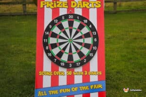 A colorful dartboard game sign with the text "Prize Darts," inviting players to score over 50 points with three darts. Fun fair atmosphere.