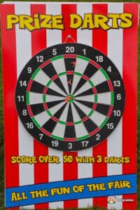 Colourful dartboard game sign with red and white stripes. Fairground darts fete game setup on lush grass.