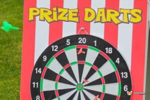 A colorful 'Prize Darts' game board with a dartboard displaying red and black sections, green accents, and several darts stuck in the board.