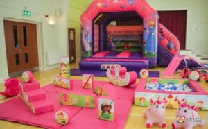 A cheerful play area showcasing a bouncy castle, slide, and toys, all part of a princess soft play package for kids.