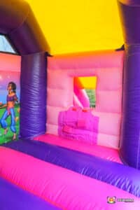A girl plays on a vibrant purple and pink inflatable bouncer, showcasing a fun and energetic outdoor activity.