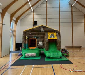 A fun bouncy castle with a front slide, featuring bright farm animal artwork in a playful farmyard theme.