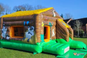 A lively bouncy castle showcasing a front slide and adorned with cheerful farm animal designs in a farmyard setting.