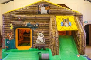 A colorful bouncy castle featuring a front slide and farmyard theme with various farm animal artwork.