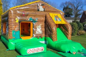 A cheerful bouncy castle with a front slide, decorated with colorful farm animal illustrations in a farmyard theme