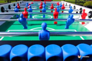 A close-up of a foosball table featuring red and blue player figures, with a green playing field visible in the background.
