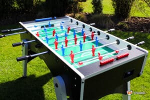 A foosball table in a grassy area, featuring red and blue player figures on a green pitch, with black and silver accents.