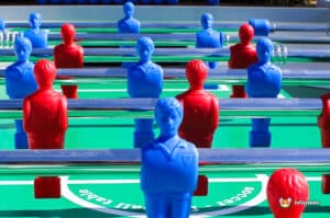 A vibrant foosball table featuring blue and red player figures arranged on a bright green field, with shiny metallic rods.