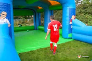 A man dressed in red plays soccer in a bouncy castle, participating in a fun football speed game