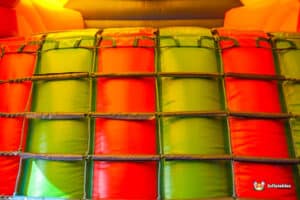 Colorful inflatable wall featuring alternating red and green panels, secured with rope and designed for recreational use.