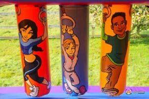 Three colorful inflatable pillars showcasing characters engaged in various athletic activities set against a grassy background.