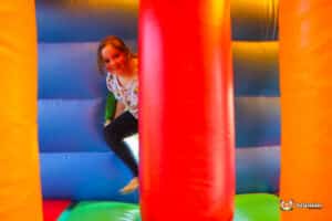 A child playfully navigates through colorful inflatable pillars in a bouncy castle. Bright blue, red, and yellow walls surround them.