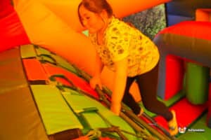 A child climbs a colorful inflatable slide, surrounded by vibrant orange, red, and green surfaces in a playful bounce house setting.