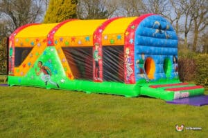 A colourful inflatable fun run 1 with cartoon characters and star designs, set on green grass in a sunny outdoor environment.