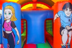 A colorful inflatable bounce house featuring cartoon characters engaged in athletic activities, surrounded by vibrant orange, blue, and green colors.