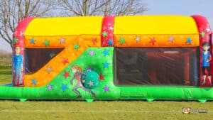 A colourful inflatable fun run 2 adorned with stars and playful character illustrations, set on a grassy field under clear skies.