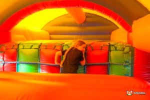 A child plays inside a colorful inflatable bounce house, navigating vibrant red and green cushions under a bright, yellow ceiling.