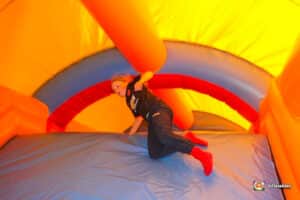 A child in dark clothing plays on a colorful inflatable bounce house, surrounded by vibrant yellow, blue, and red walls.