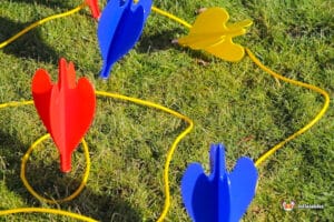 Colorful plastic toy rockets in red, blue, and yellow are arranged on green grass with yellow cords connecting them.