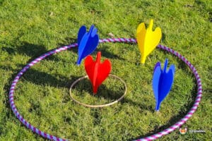 Colourful giant garden darts in red, blue, and yellow positioned within a hula hoop on green grass, ready for a game.