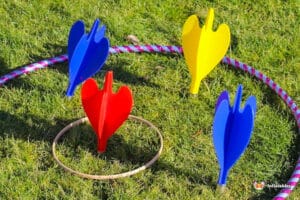 Colorful toy darts in red, blue, and yellow are arranged around a hula hoop on green grass, creating a fun outdoor game setup.