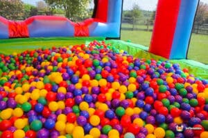 A colorful ball pit filled with red, yellow, green, purple, and blue balls inside a bouncy castle, surrounded by greenery.