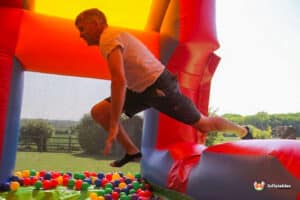 A person jumps playfully in a colorful inflatable bounce house filled with vibrant balls, surrounded by a sunny outdoor landscape.