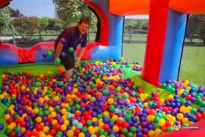 A vibrant ball pit filled with colorful balls in a bouncy castle, surrounded by greenery and sunshine.
