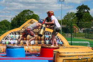 Two boys playfully battling on a gladiator duel inflatable, using foam sticks in a fun and energetic setting.
