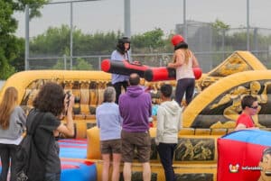 Two girls having fun on a gladiator duel inflatable, playfully competing with foam sticks in a lively atmosphere.