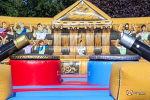 An inflatable bouncer featuring a gladiator duel theme, with colorful designs.