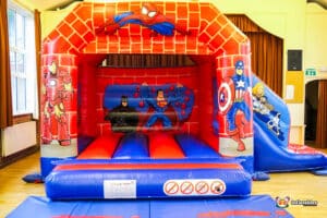 A hero-themed bouncy castle featuring Spider-Man like graphics, designed for bouncing and sliding fun for children.