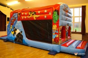A colourful superhero-themed fun run features iconic characters like Batman, Superman, and Wonder Woman on a vibrant inflatable structure.