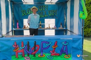A colourful hoopla side stall with a bright blue and white striped canopy, showcasing various whimsical objects on a blue table.