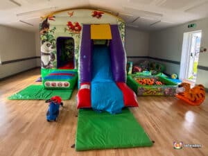 A lively play area equipped with a slide, jungle gym, tiger rocker, and soft play structures for children's enjoyment.