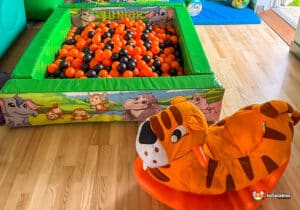 A tiger rocker beside a ball pit filled with orange balls, creating a fun play area.
