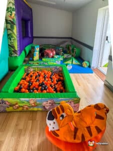 A jungle-themed ball pit with orange and black balls, featuring a stuffed tiger rocker for children's playtime.