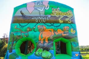 A colorful jungle-themed inflatable with cartoon animals, including an elephant, leopards, monkeys, and a tiger, inviting play for kids.