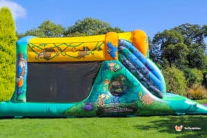 Colourful inflatable jungle-themed fun run with a slide, featuring playful monkeys and other animals against a bright sky background.