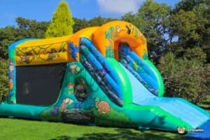 Colourful inflatable jungle fun run with a slide, featuring jungle-themed graphics and surrounded by lush greenery under a blue sky.
