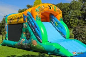 A colourful inflatable jungle fun run with a slide, featuring jungle animal designs, set in a green grassy area under a clear blue sky.