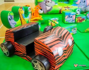A children's party featuring a zebra-themed car amidst a jungle soft play area, filled with colorful decorations and fun activities.