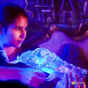 A person holds a glowing, translucent toy gun, with vibrant blue lights, against a colorful graffiti background.