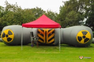 A large Laser Tag Arena structure resembling a radioactive symbol, with a red canopy, set in a grassy area among trees.
