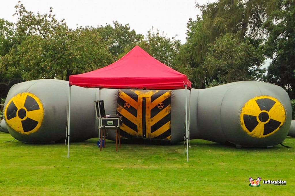 A large Laser Tag Arena structure resembling a radioactive symbol, with a red canopy, set in a grassy area among trees.