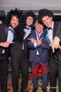 Three men in suits pose with a man in a wig, featuring the Magic Photo Mirror with Kevin Keegan in the background.
